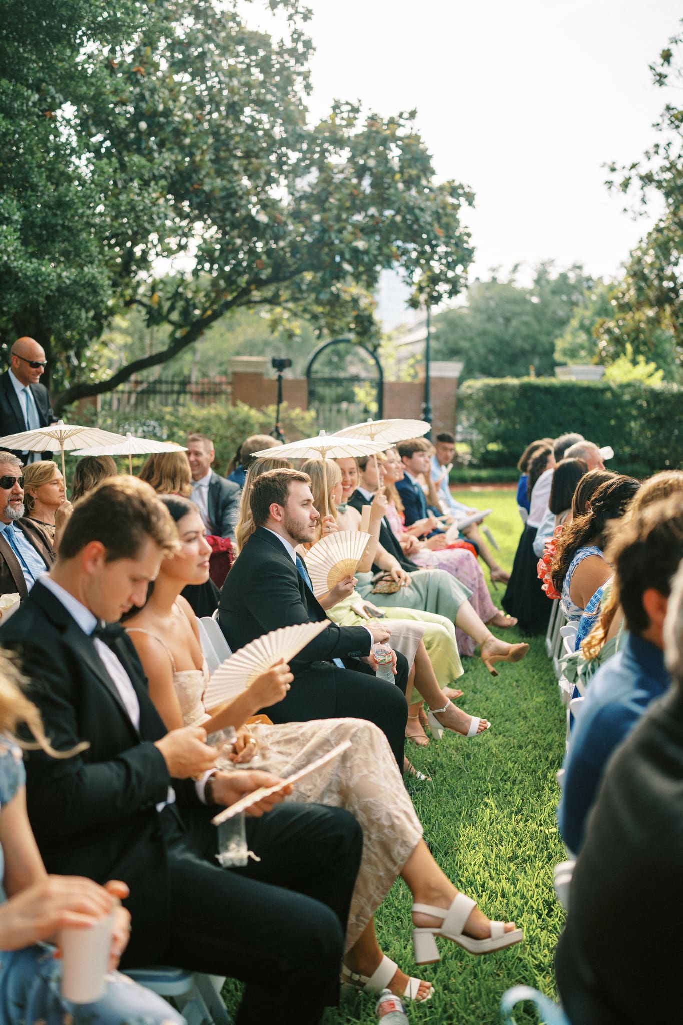 wedding guests holding parasol umbrellas at an outdoor wedding ceremony at the junior league of Houston