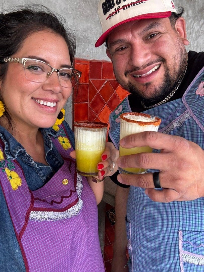Happy couple in aprons toasting with micheladas during an Oaxaca cooking class