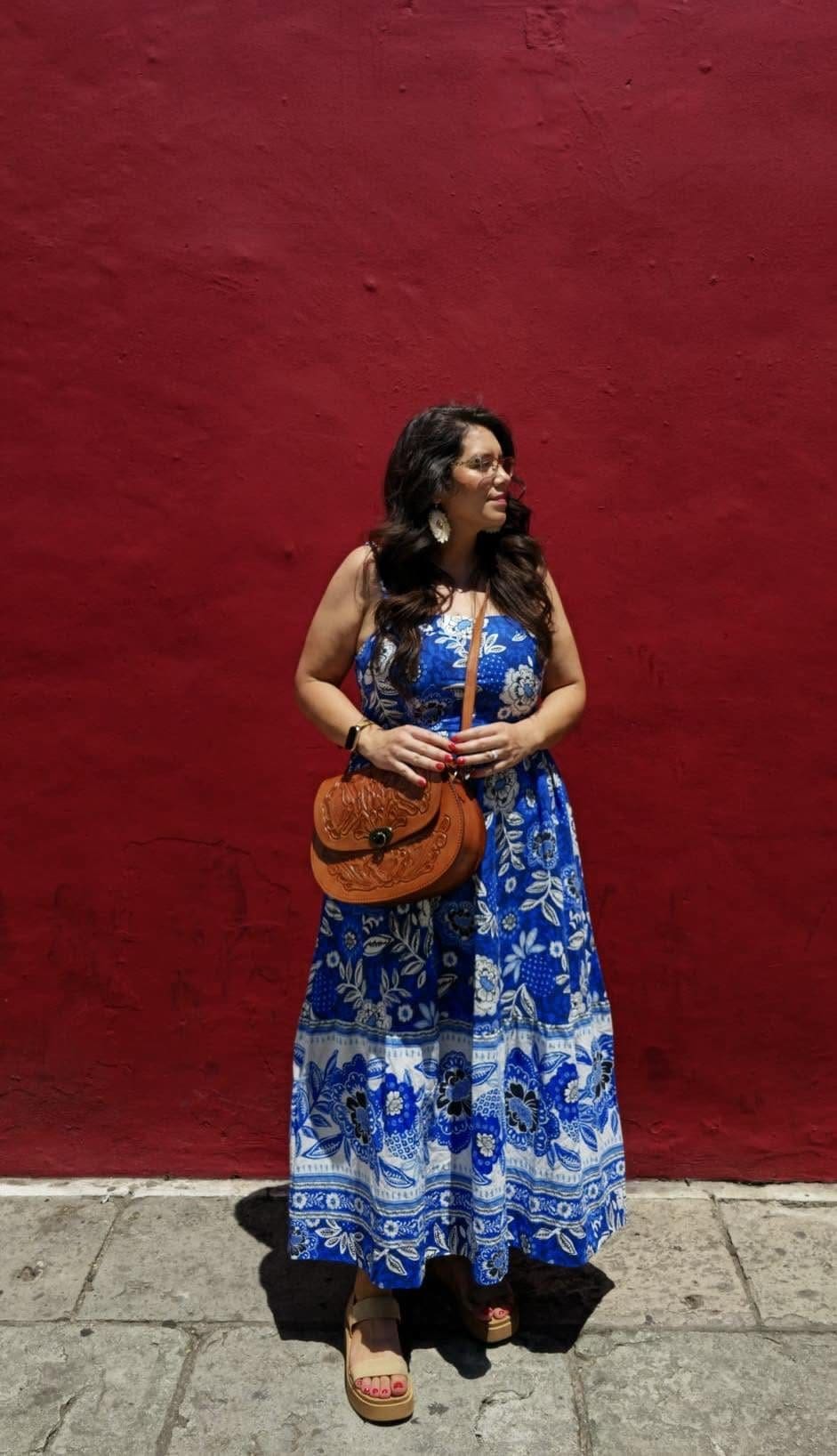 Woman in a blue floral dress posing against a deep red wall in Oaxaca City, Mexico