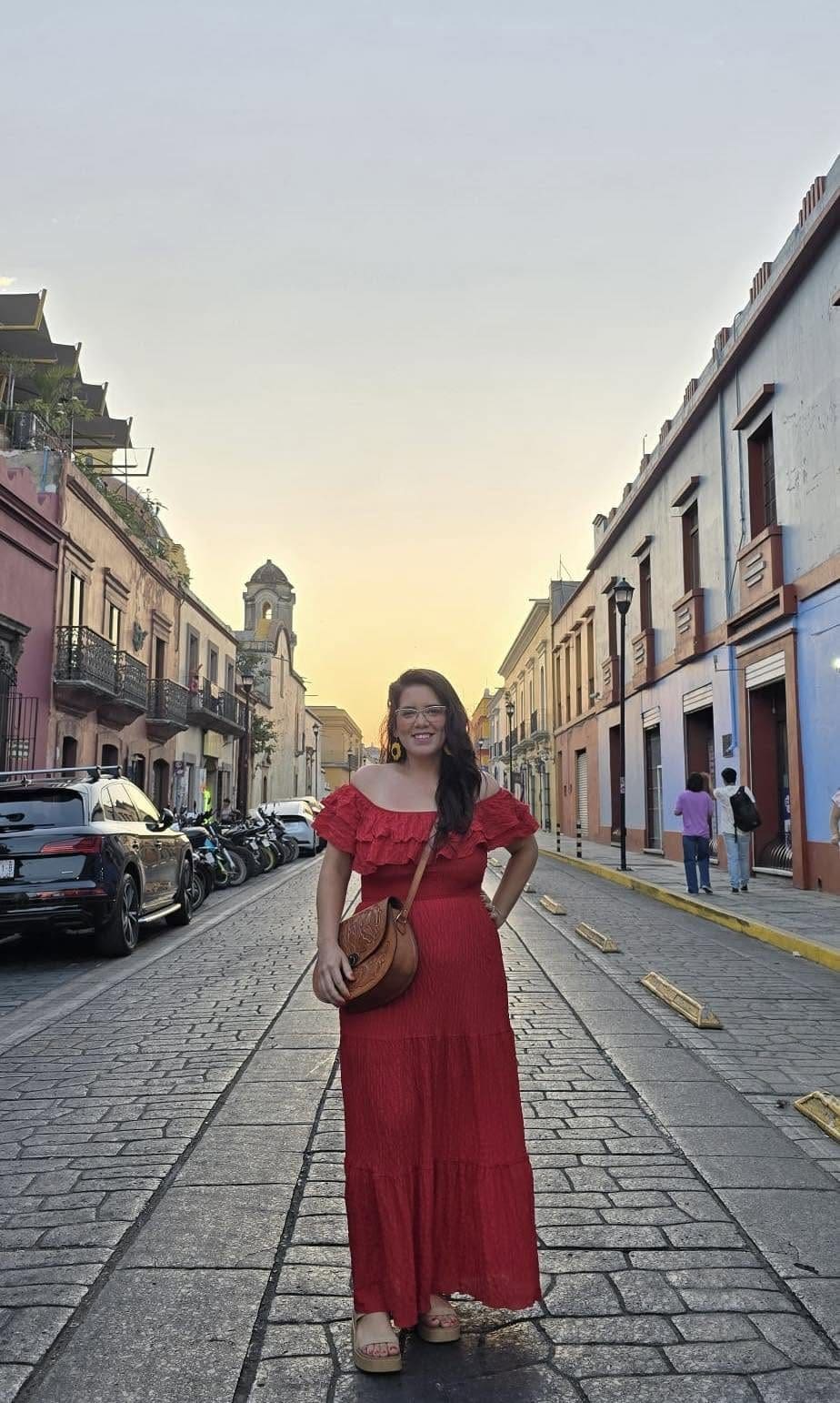 Woman in a red dress standing on a cobblestone street in Oaxaca City at golden hour